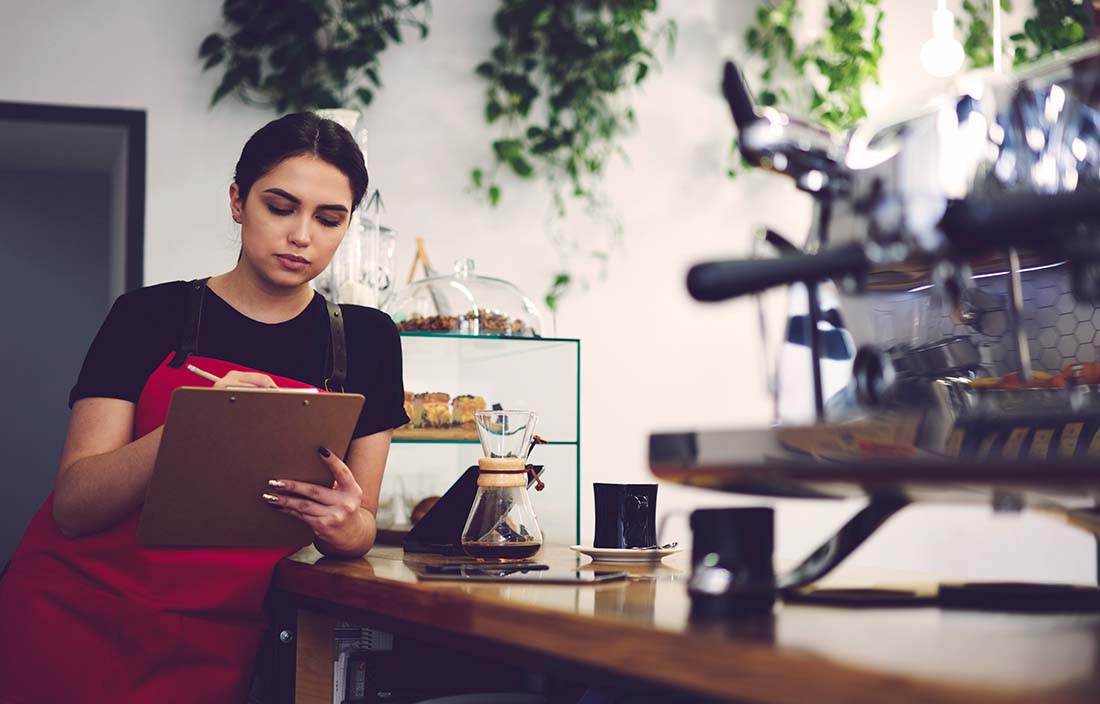 Image of a female barista holding a clipboard behind the coffee shop counter.
