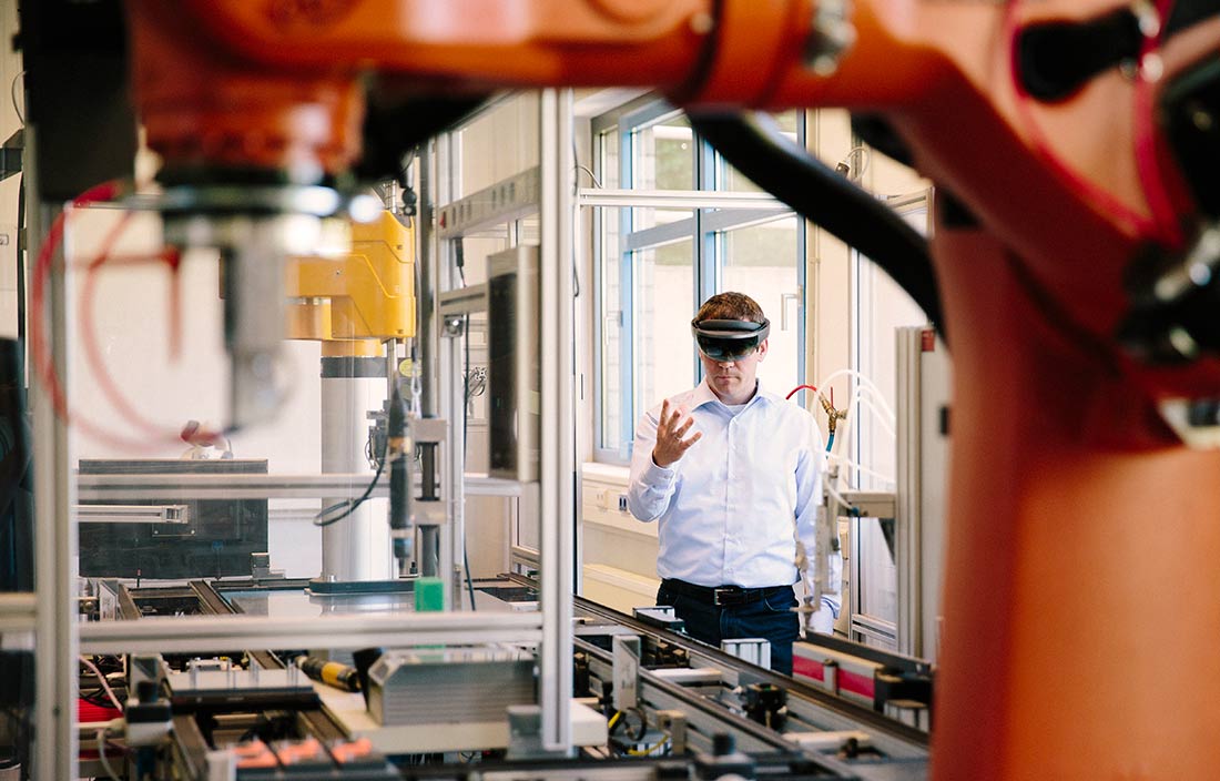 Businessman in a factory workshop wearing VR goggles and holding hands up.