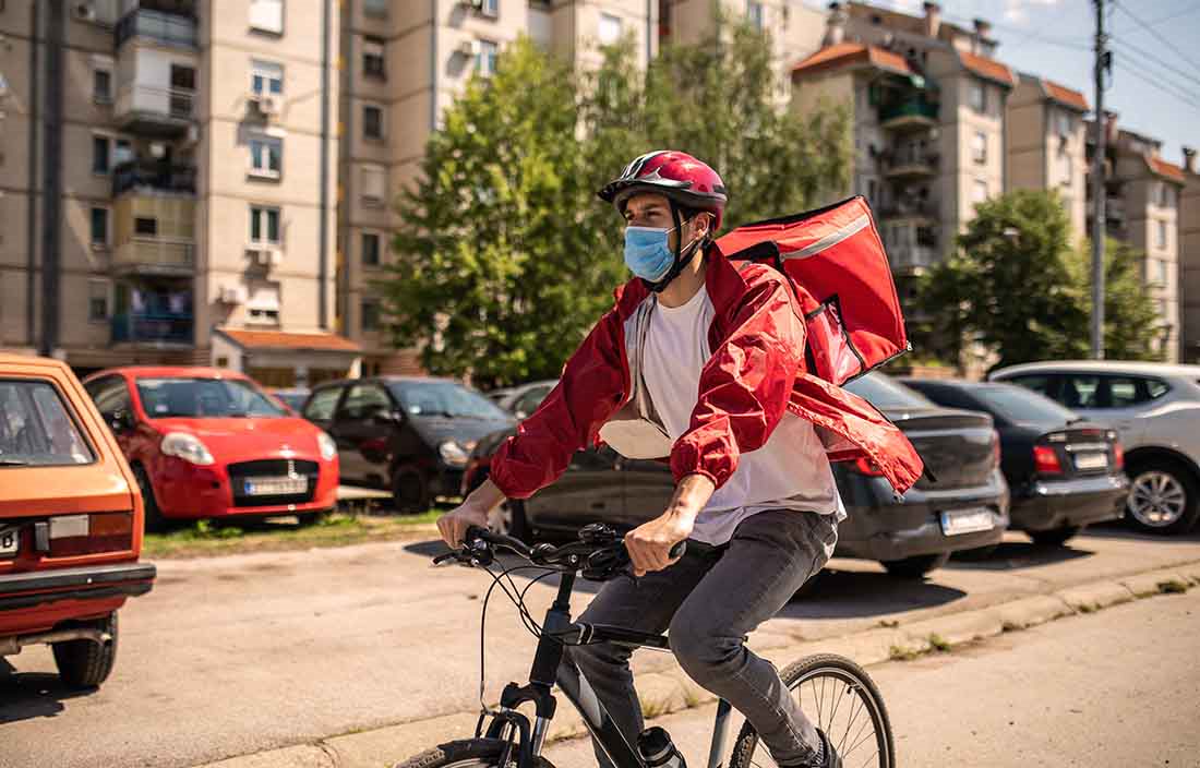 Delivery worker riding a bike while wearing a protective facemask.