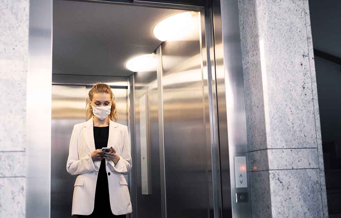Business professional wearing a protective facemask while standing in an elevator.