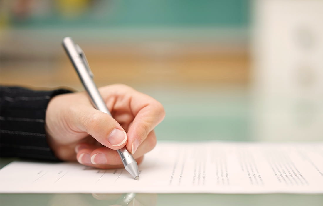 Image of a hand with a pen signing a document