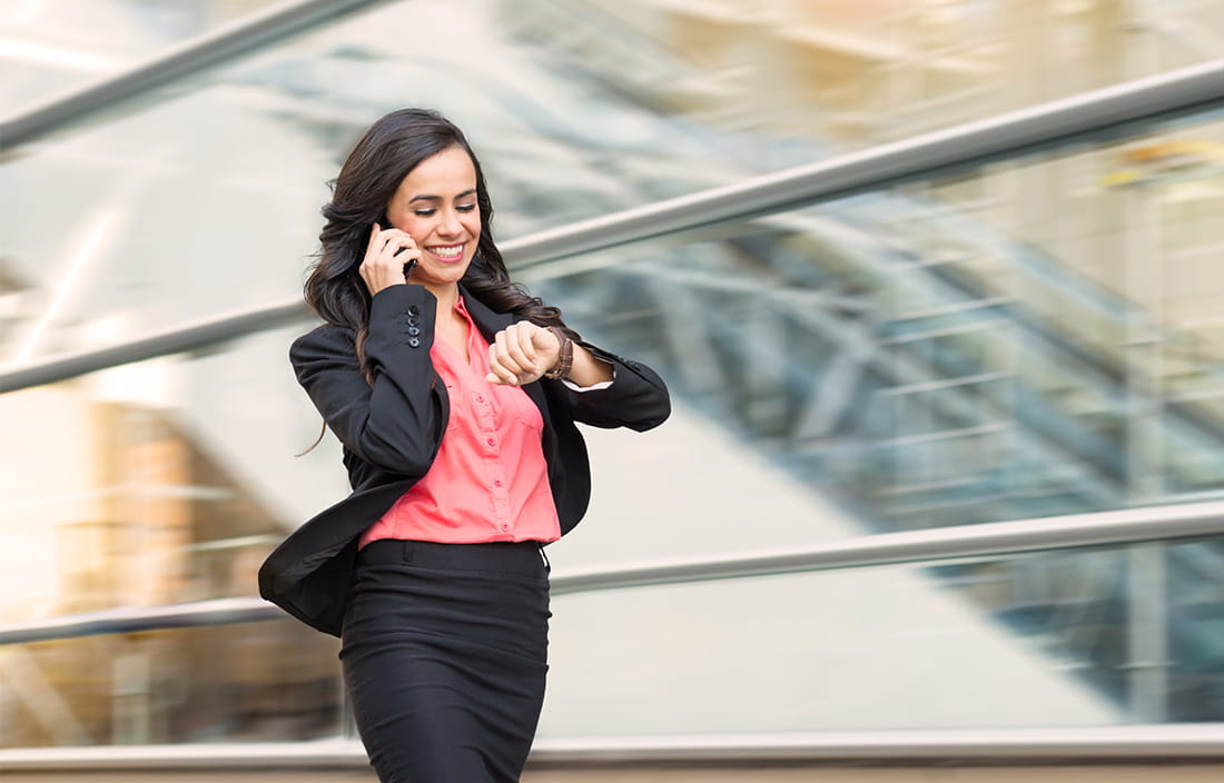 image of woman looking at her watch and talking on the phone while walking