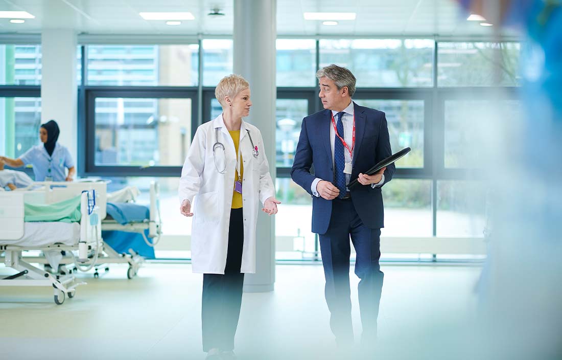 A doctor and a business professional walking through a hospital.