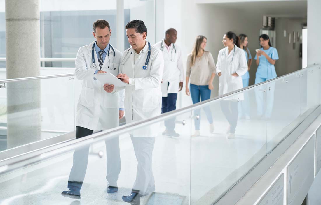 Two doctors walking across a walkway together reviewing charts.