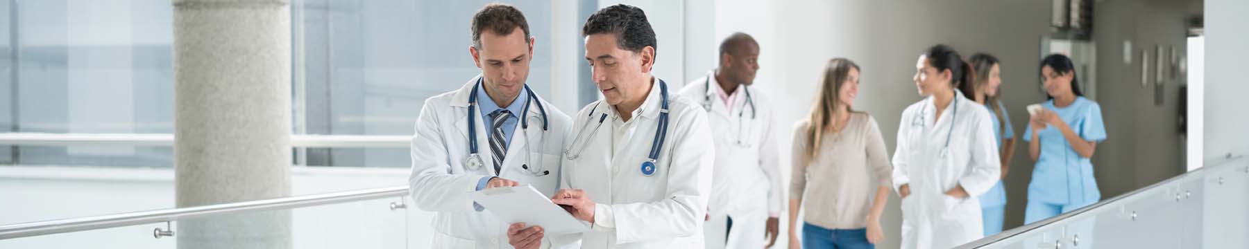 Two doctors walking across a walkway together reviewing charts.