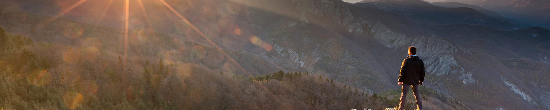 A man standing on a mountain ridge looking at a sunset.