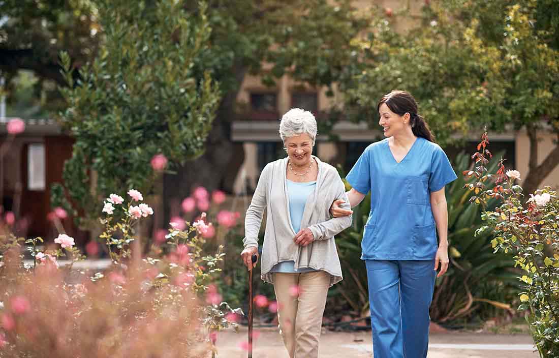 Senior care worker walking with an elderly patient in a garden.
