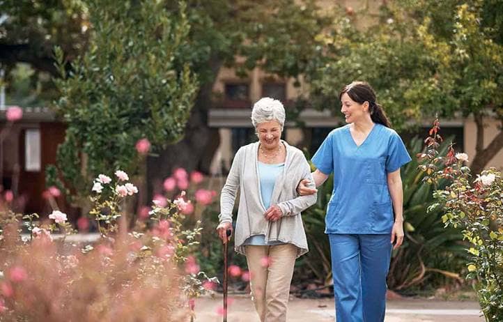 Senior care worker walking with an elderly patient in a garden.
