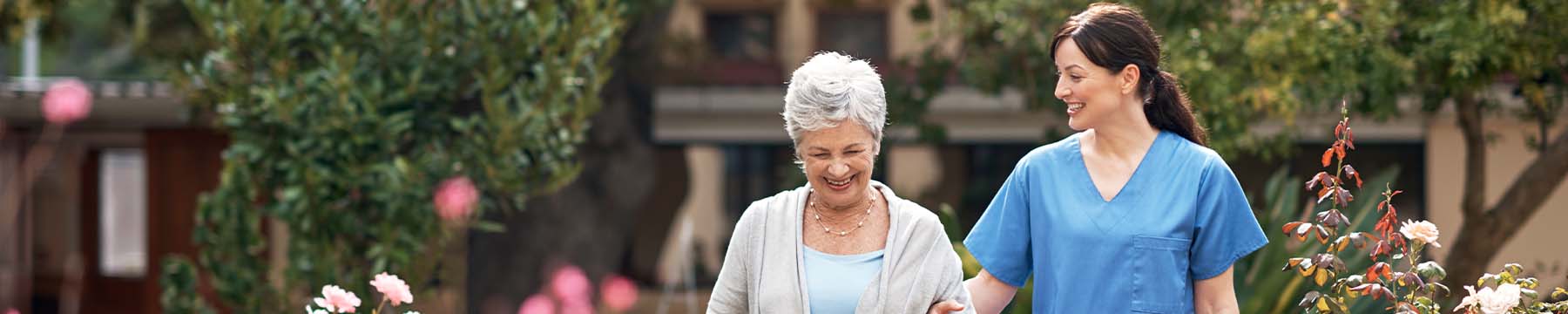 Senior care worker walking with an elderly patient in a garden.