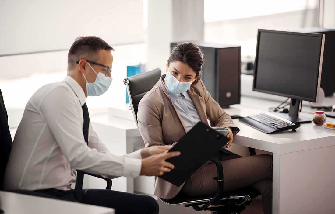 Businessman and businesswoman in the office reviewing a document while wearing facemasks.