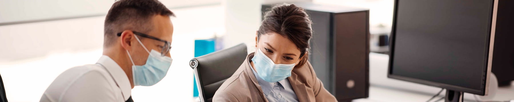 Businessman and businesswoman in the office reviewing a document while wearing facemasks.