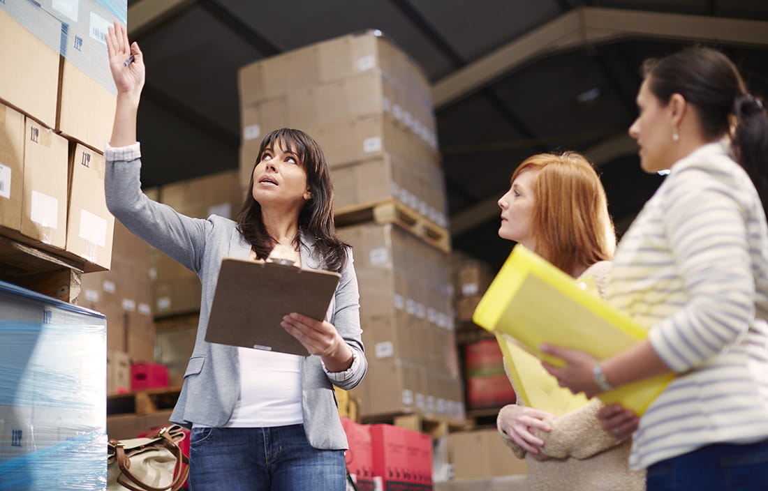 Woman with clipboard in warehouse talking to women