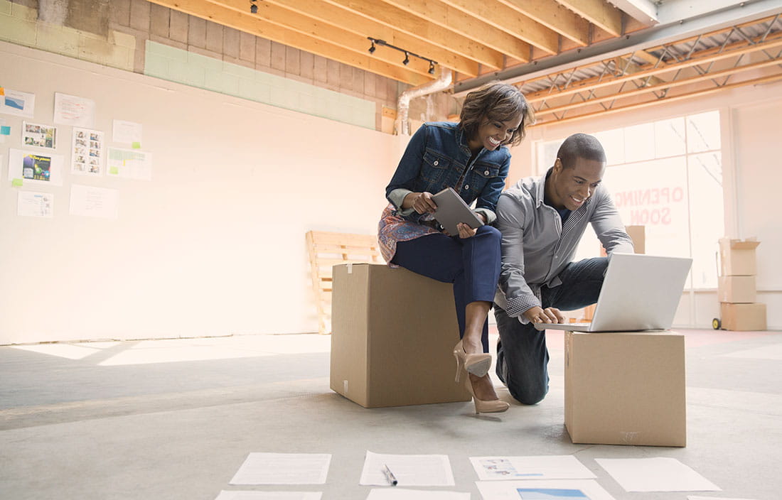 Man and woman looking at laptop in sparse room containing a few cardboard boxes.