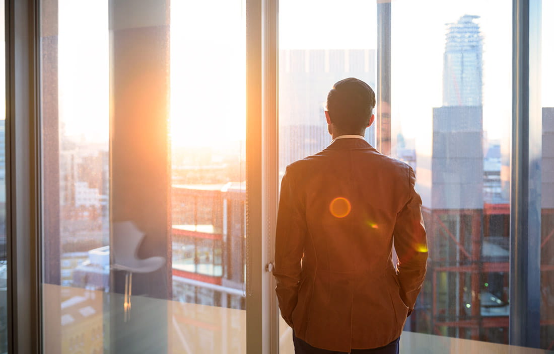 Businessman watching the sunrise from his office window