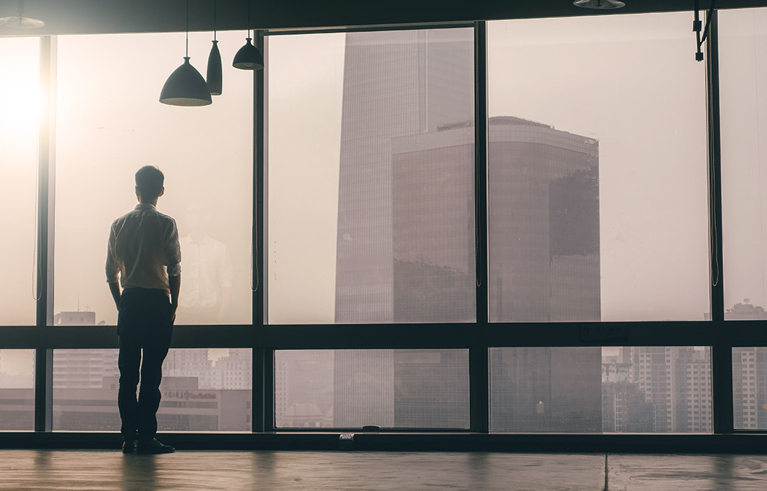 Image of man standing in front of windows looking at corporate buildings