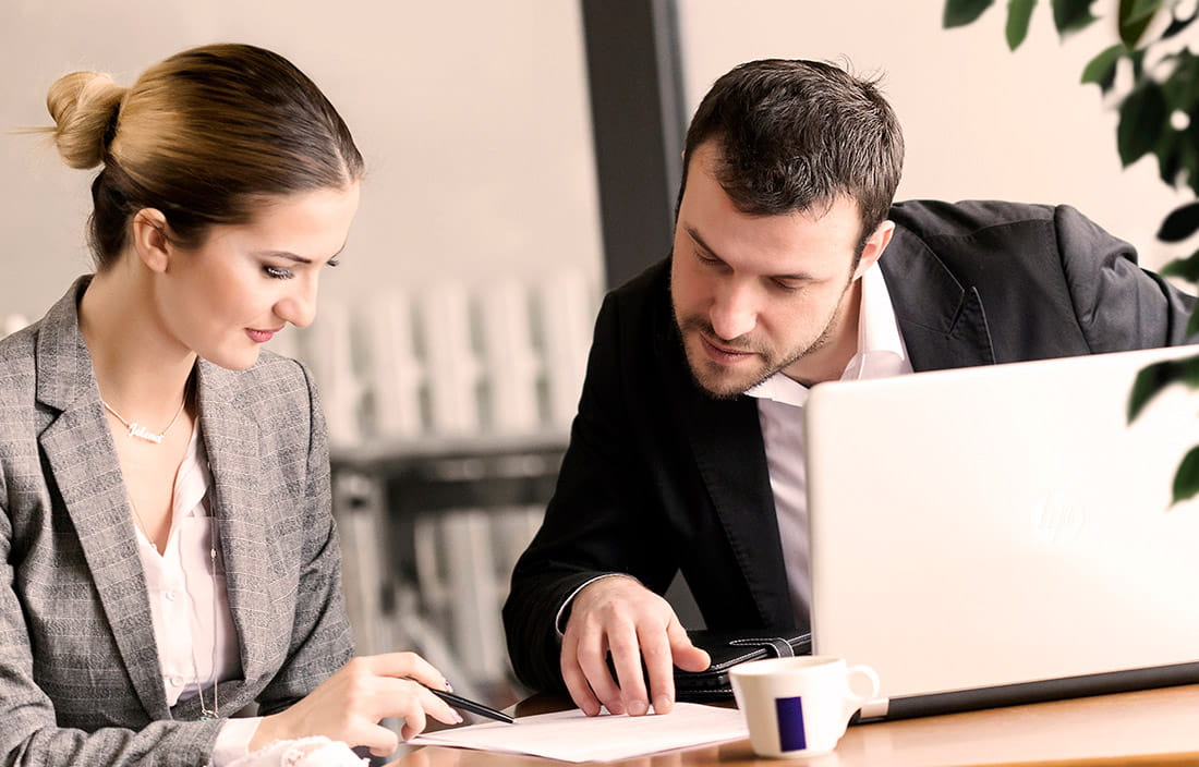 Man and woman going over paperwork at a table with a laptop