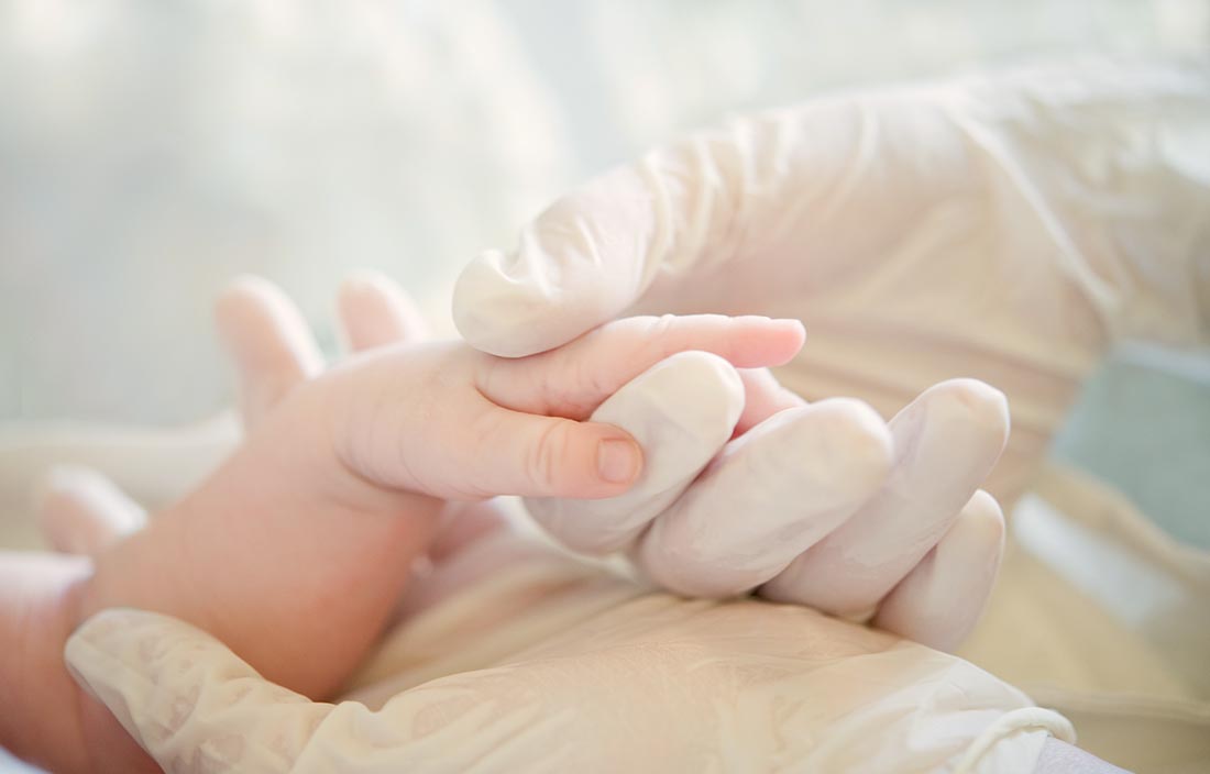 doctor's gloved hands holding a baby's hand