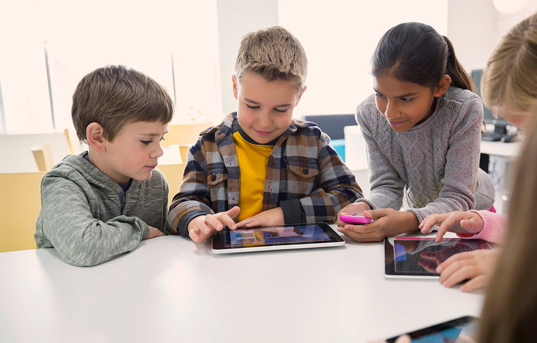 small group of kids at a school table looking a tablet device