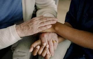 Close-up on the hands of a senior and their care provider.
