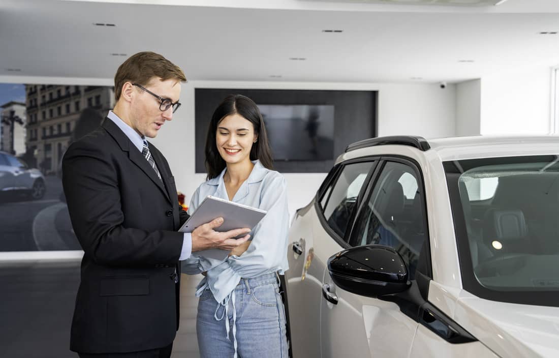 Two business professionals reviewing documents next to a car.