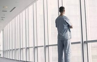 Doctor standing in a walkway looking out the window.