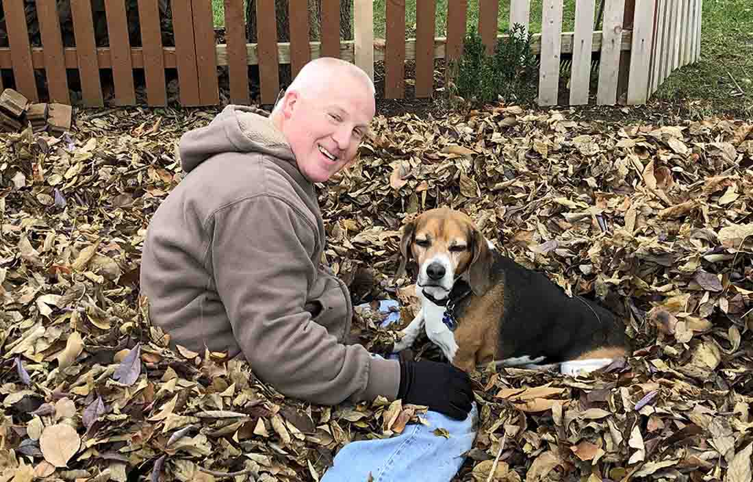 A man playing with his dog in a leaf pile.