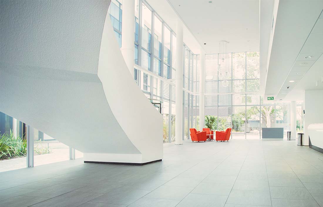 modern multi-level white office lobby with two red seats in the distance 