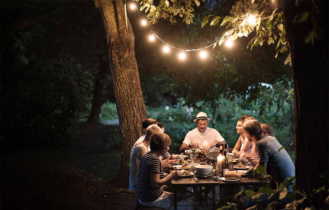Outdoor dinner with friends and family at night in backyard. string lights frame the shot and add light to the table 