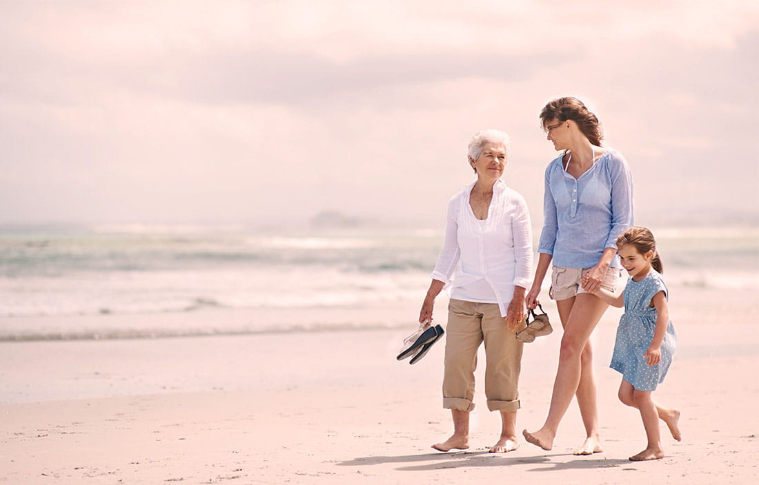 grandmother, mother and child walk together on the beach