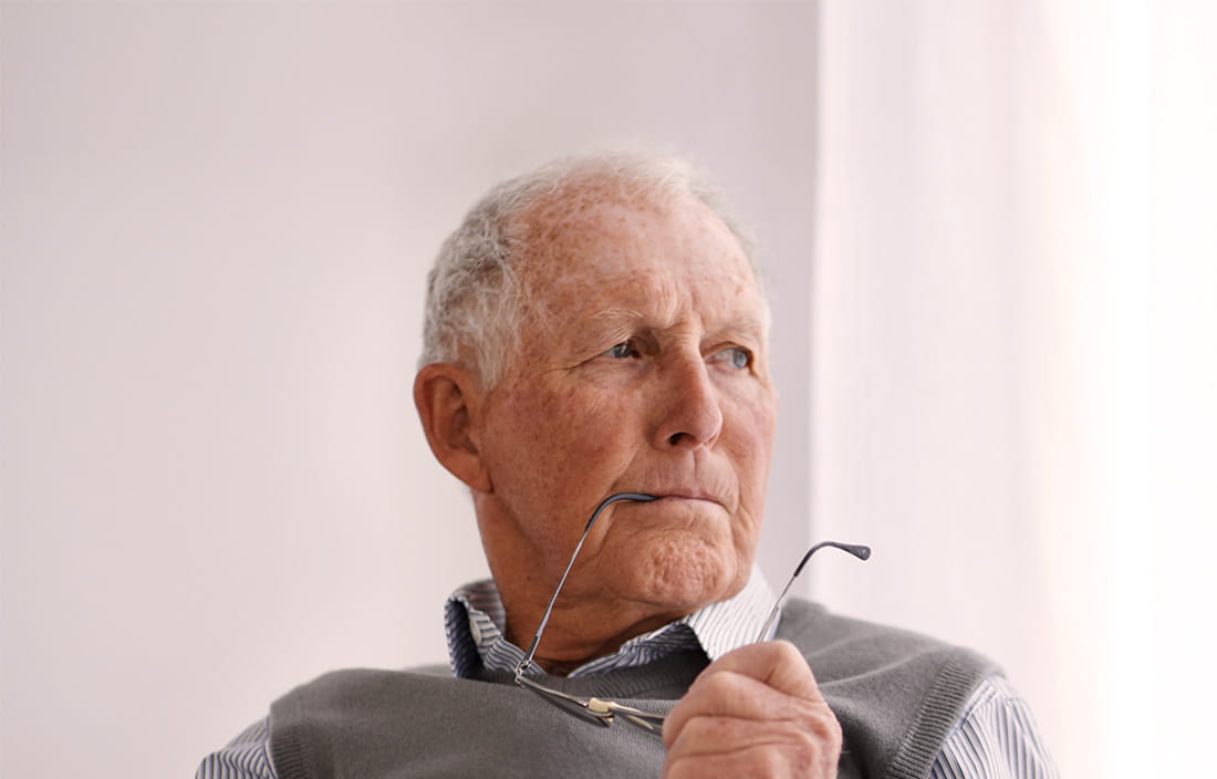 Older gentleman thinking with his glasses arm in his mouth 