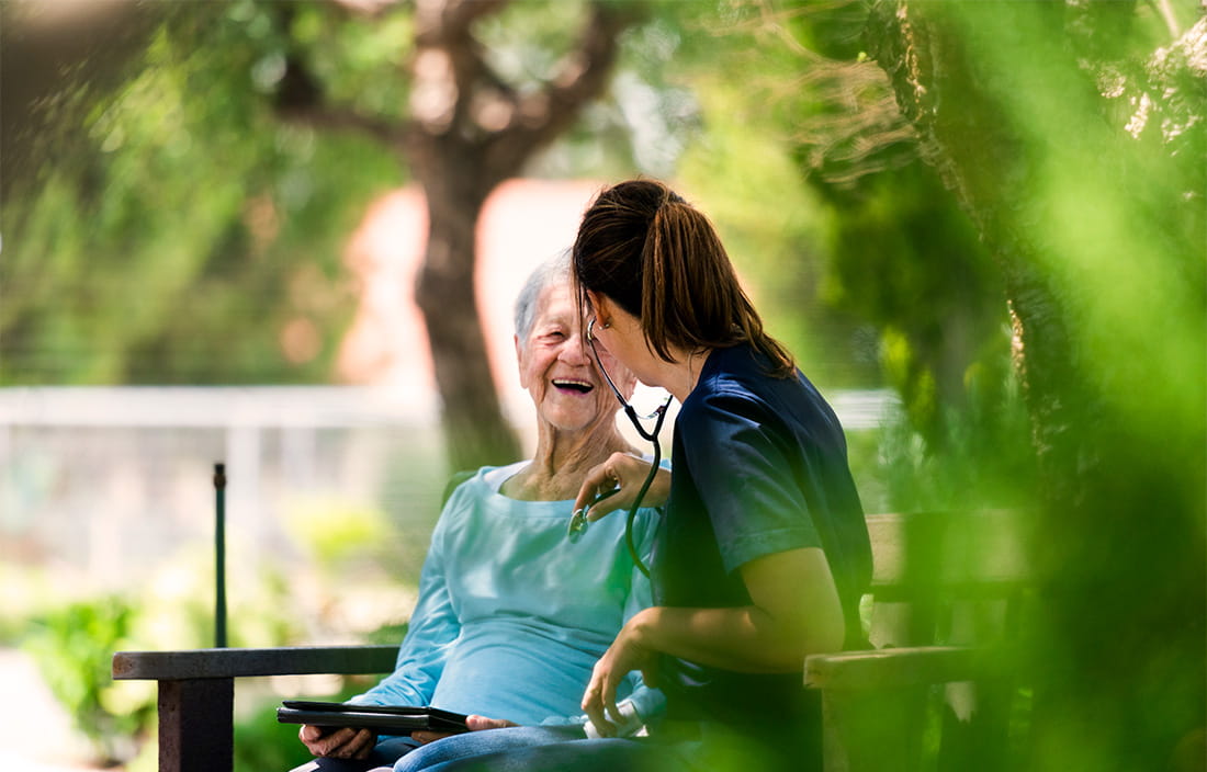 Senior mother and female care taker cheerfully talking on a park bench 