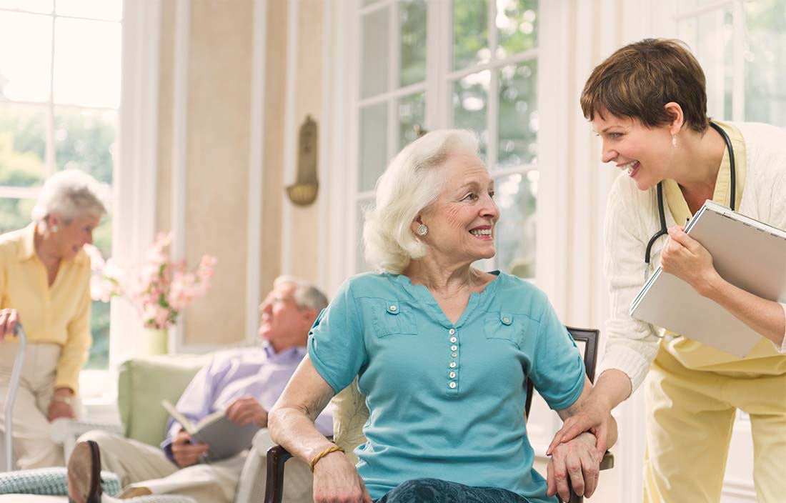 Senior woman cheerfully speaking with her female caretaker in a senior living facility 