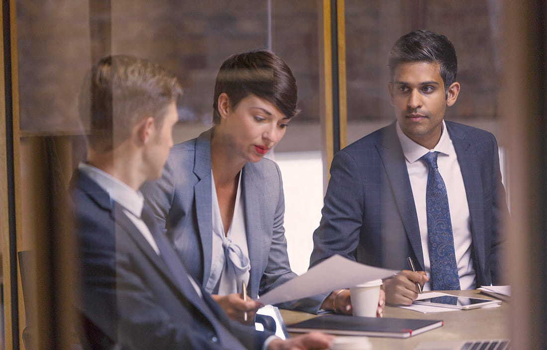 Two men and a woman sitting at a conference table looking over documents