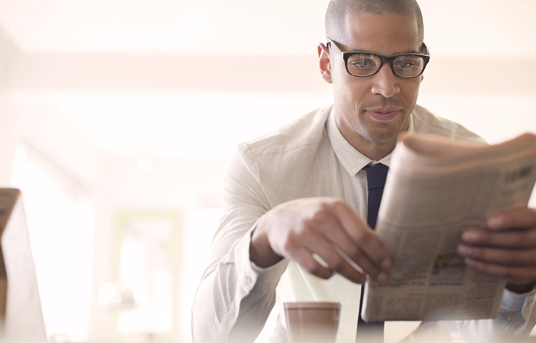 Business man sitting at a counter with a cup of coffee reading a newspaper