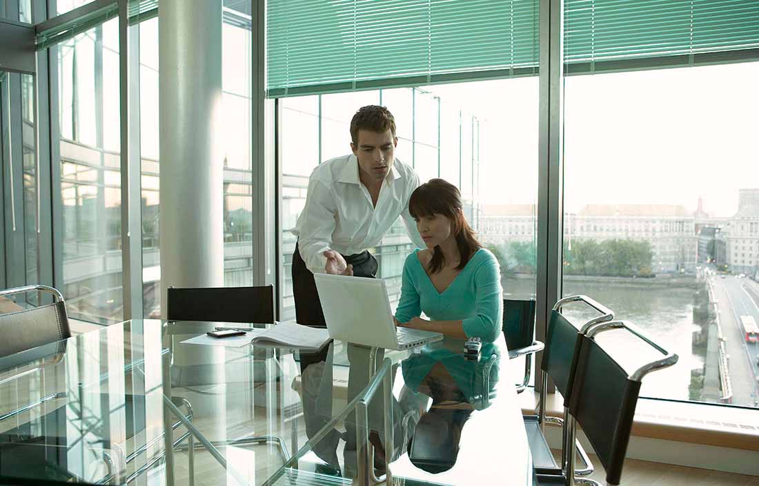 Man and woman looking at a laptop in a glass office