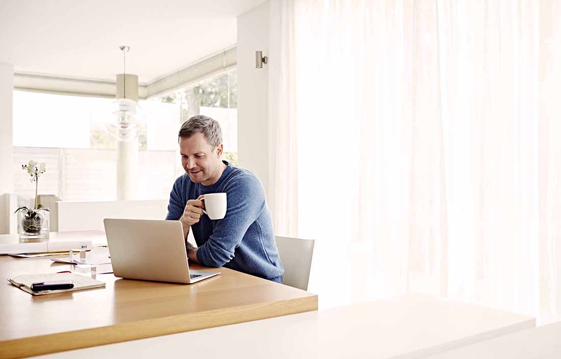 Man sitting at a table drinking coffee and looking at his laptop