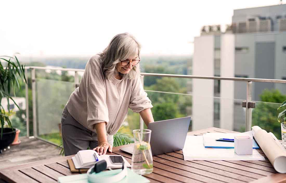 Elderly person leaning over a wooden table looking at a laptop screen.