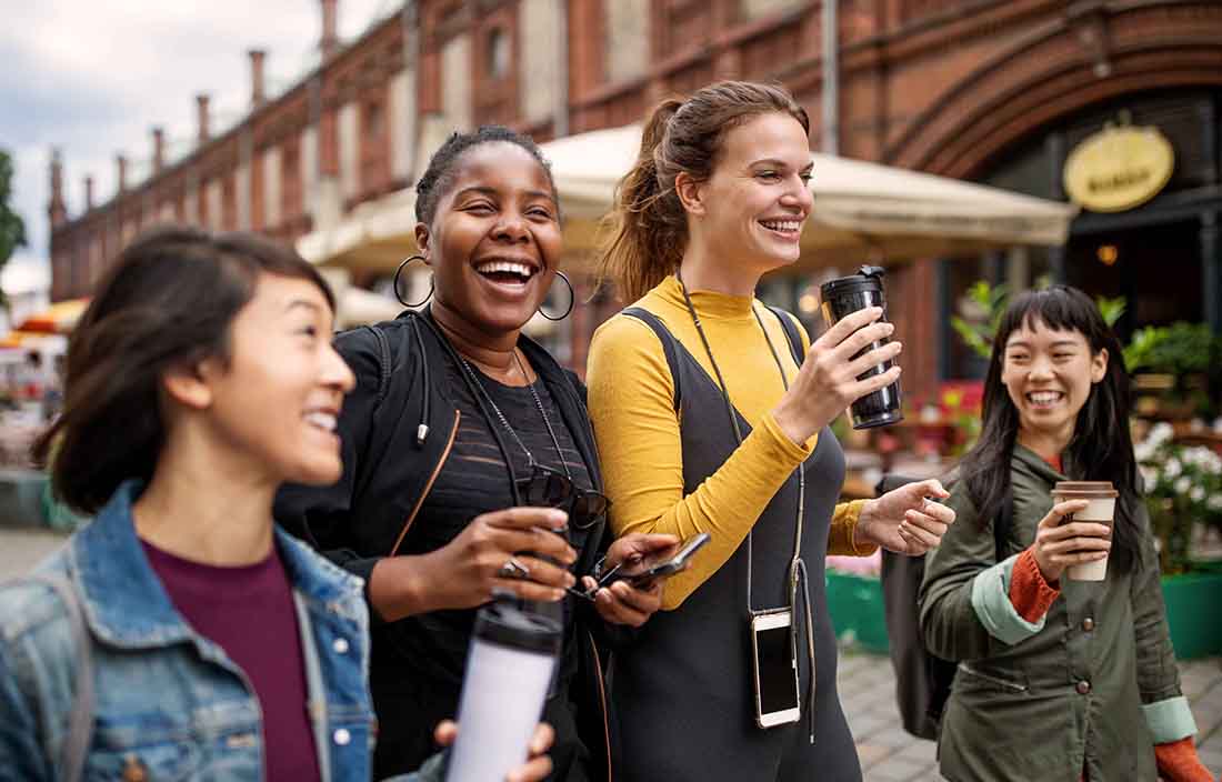 Business professionals in casual clothing walking down a street drinking coffees.
