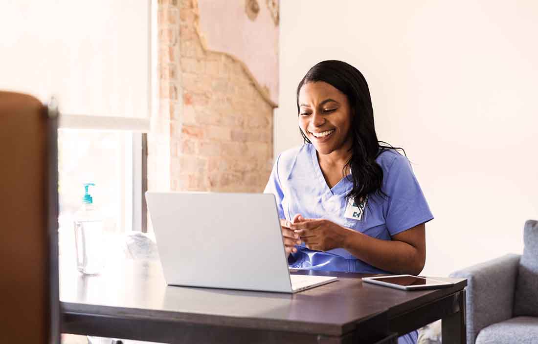Nurse professional sitting in front of her laptop computer smiling.