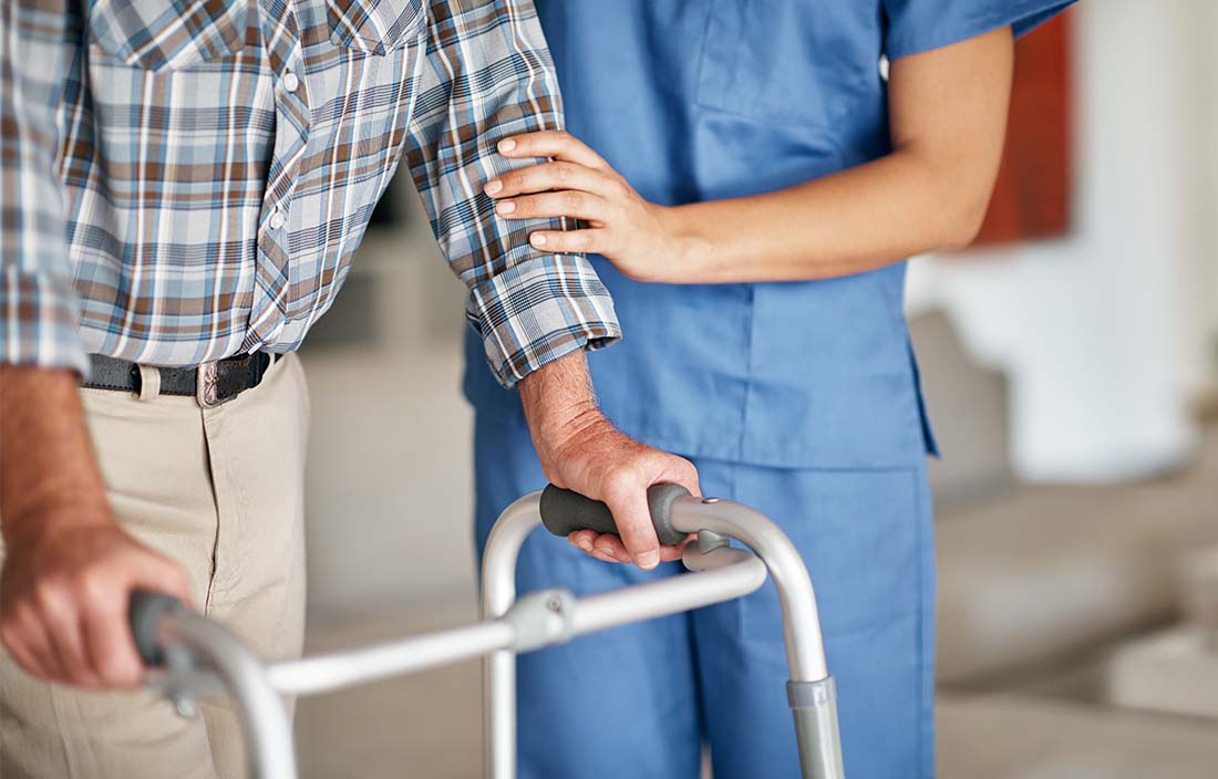 Nurse helping an elderly person walk with a mobility device.