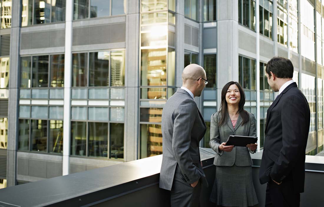Three business professionals chatting on roof deck.