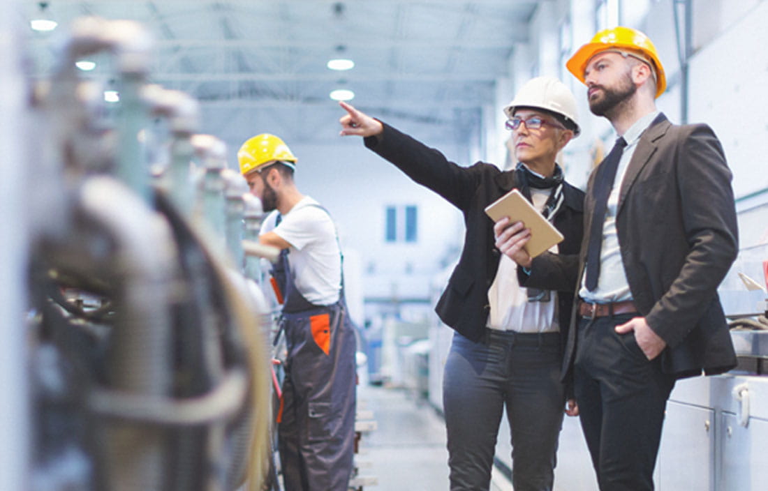 Business professionals in a warehouse wearing hard hats.