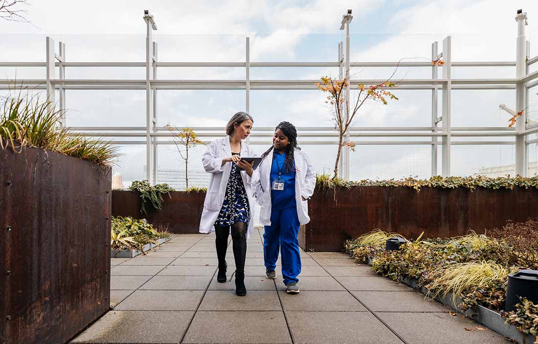 Female doctors talking while walking on rooftop of hospital.