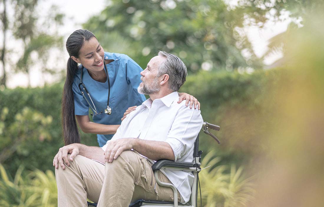 Nurse smiling and talking to a senior citizen in a wheelchair. 