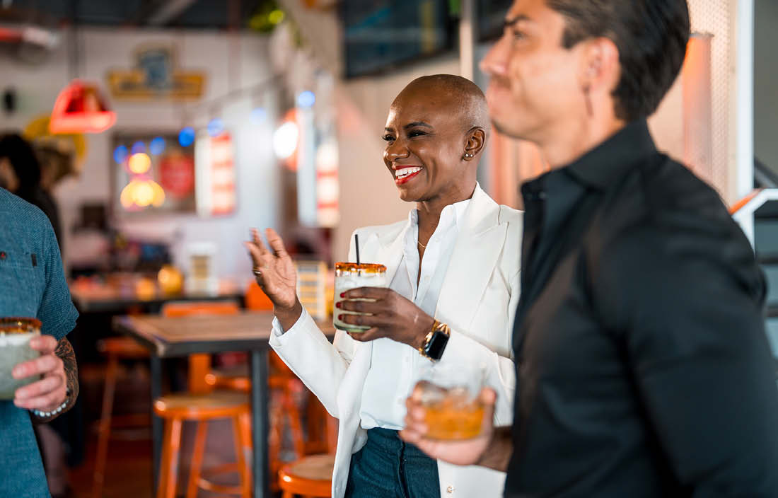 Professionals chatting indoors while holding drinks in a casual bar setting.