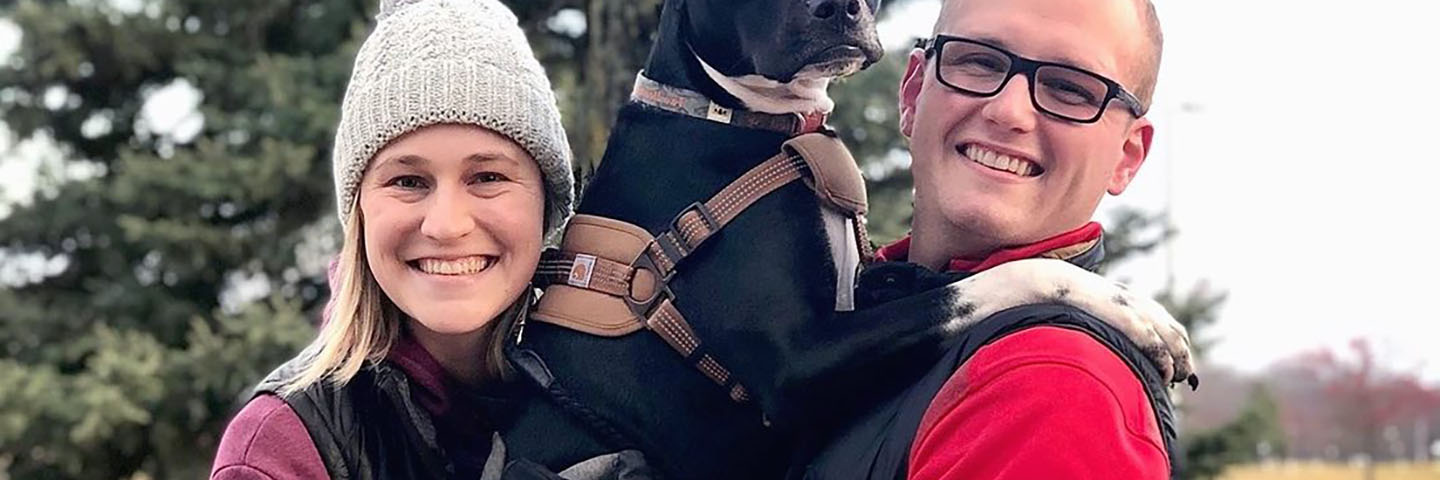 A couple posing for a photo holding their dog.