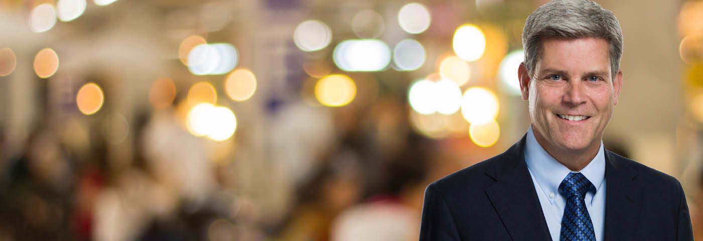 Professional photo of Jim Proppe in front of blurred brightly colored background.