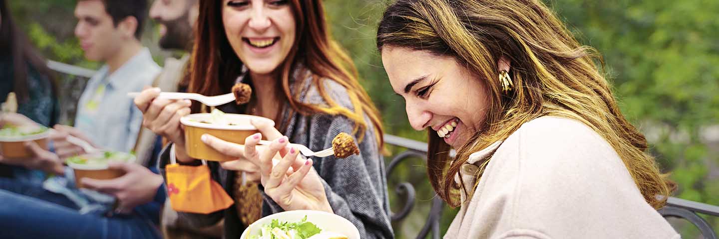 People eating falafel and salad on a park bench.