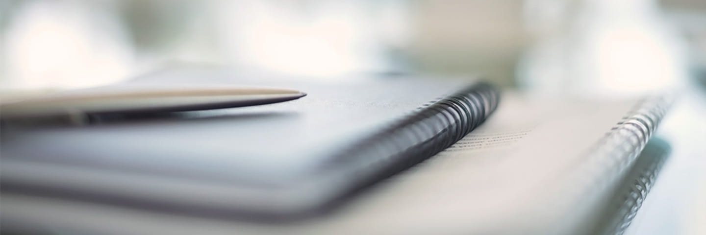 Close-up view of a notebook and pen on a desk.