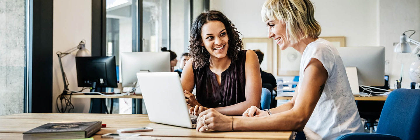 Two business professionals reviewing information on a laptop computer while smiling.